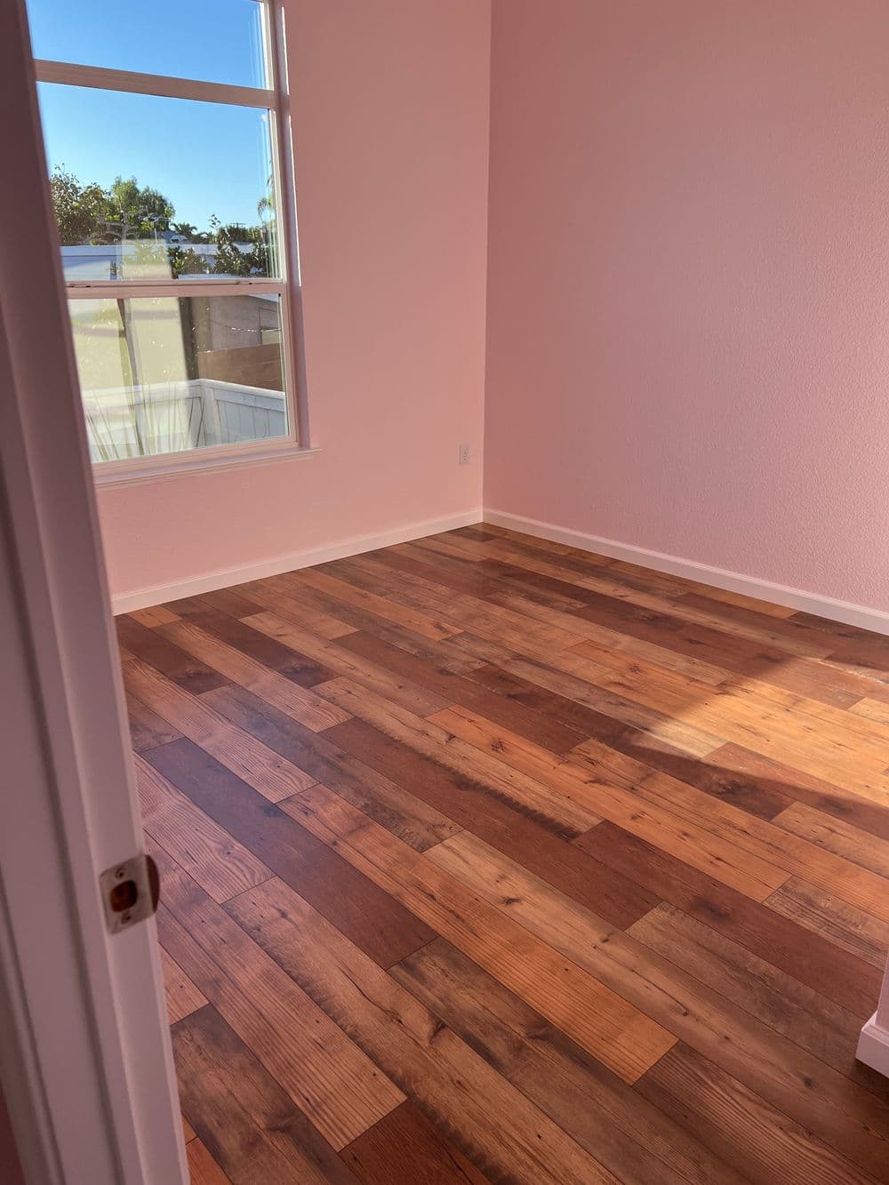Empty room with natural light, featuring brown wooden flooring and pink walls.
